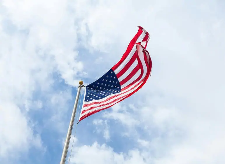 american flag on a pole with a cloudy blue sky in the background