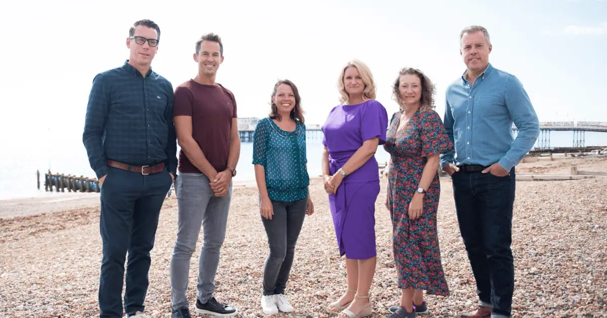 Group photo of Travel Places staff by the seaside in casual business attire.